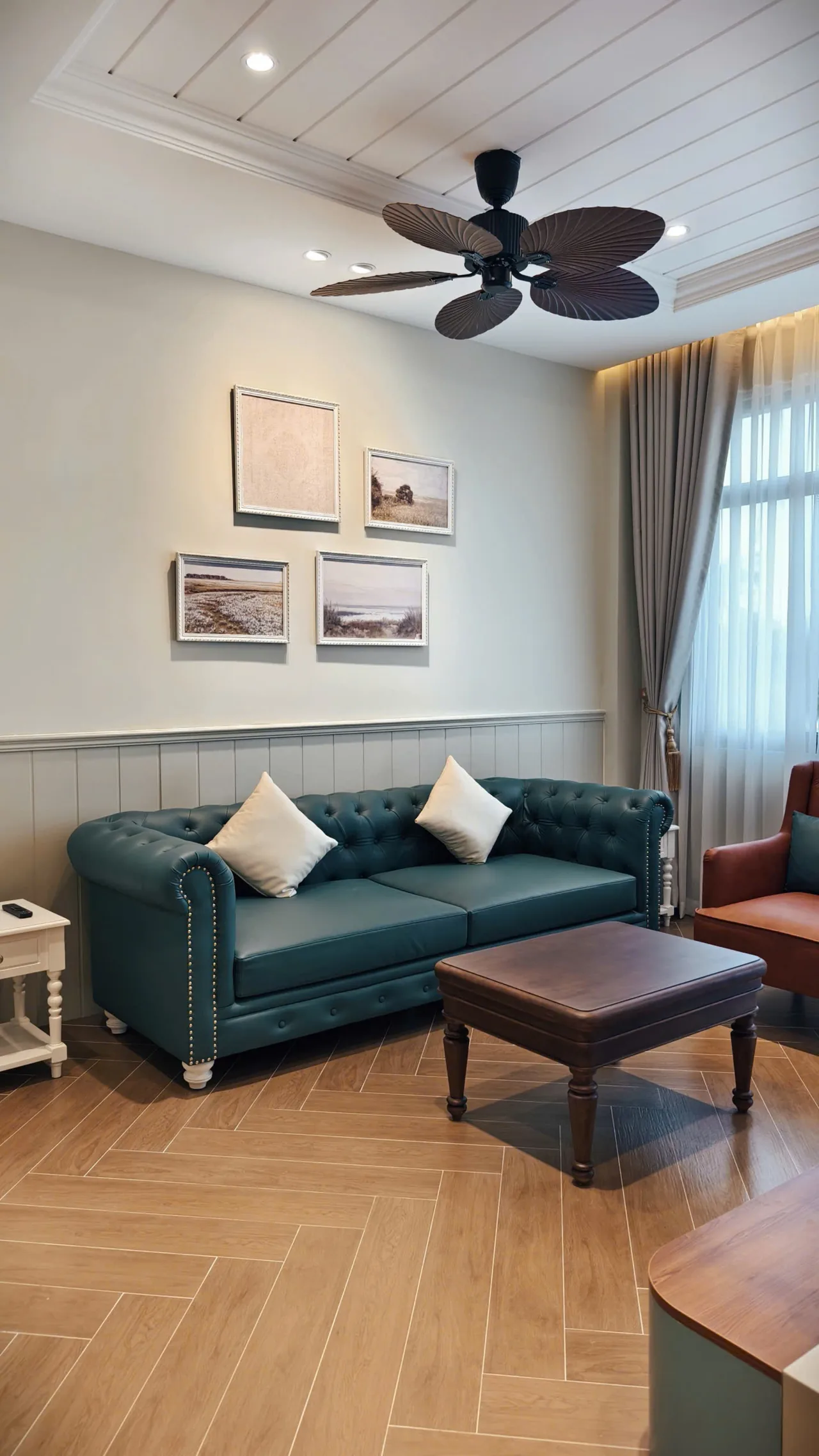 Ảnh thực tế góc sofa da xanh rêu dưới bộ tranh phong cảnh, ốp tường lam trắng và quạt trần cánh lá, căn nhà D.HOUSE bàn giao tại The Tropicana, NovaWorld Hồ Tràm