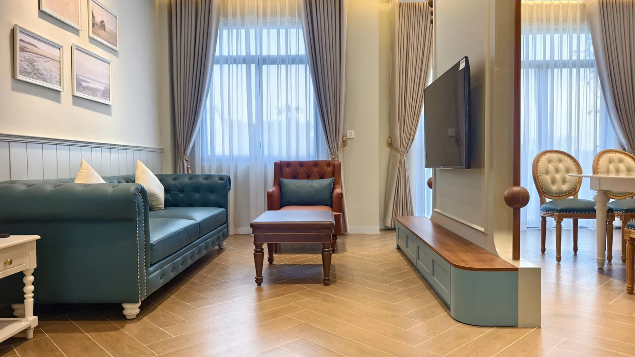 Ảnh thực tế phòng khách với sofa da xanh rêu, ghế bành nâu và vách tivi có trụ gỗ tiện ngăn sang khu ăn, căn nhà D.HOUSE bàn giao tại The Tropicana, NovaWorld Hồ Tràm