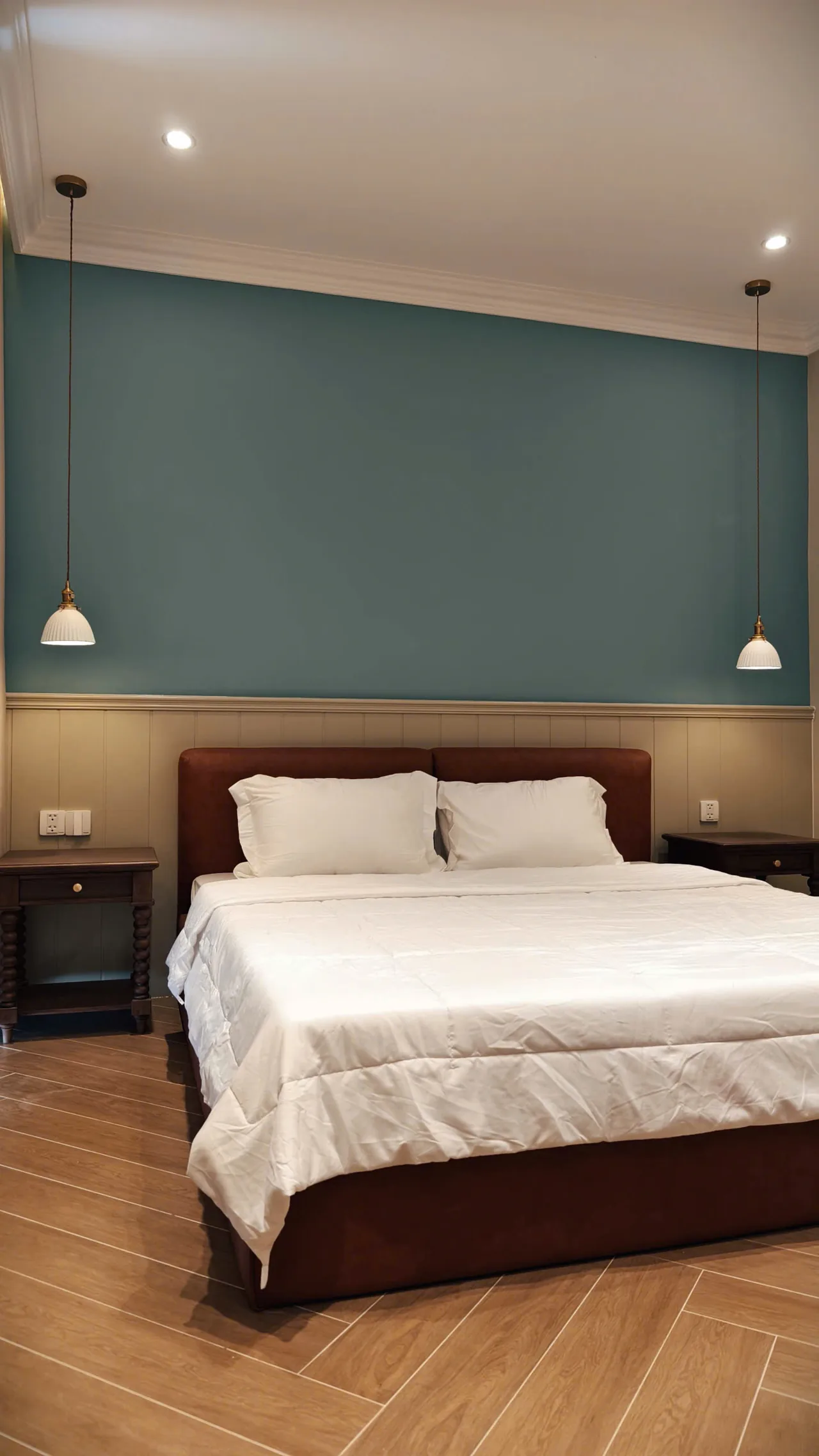 Ảnh thực tế phòng ngủ với mảng tường xanh, ốp gỗ chân tường, giường bọc nệm nâu đỏ và hai đèn thả, căn nhà D.HOUSE bàn giao tại The Tropicana, NovaWorld Hồ Tràm