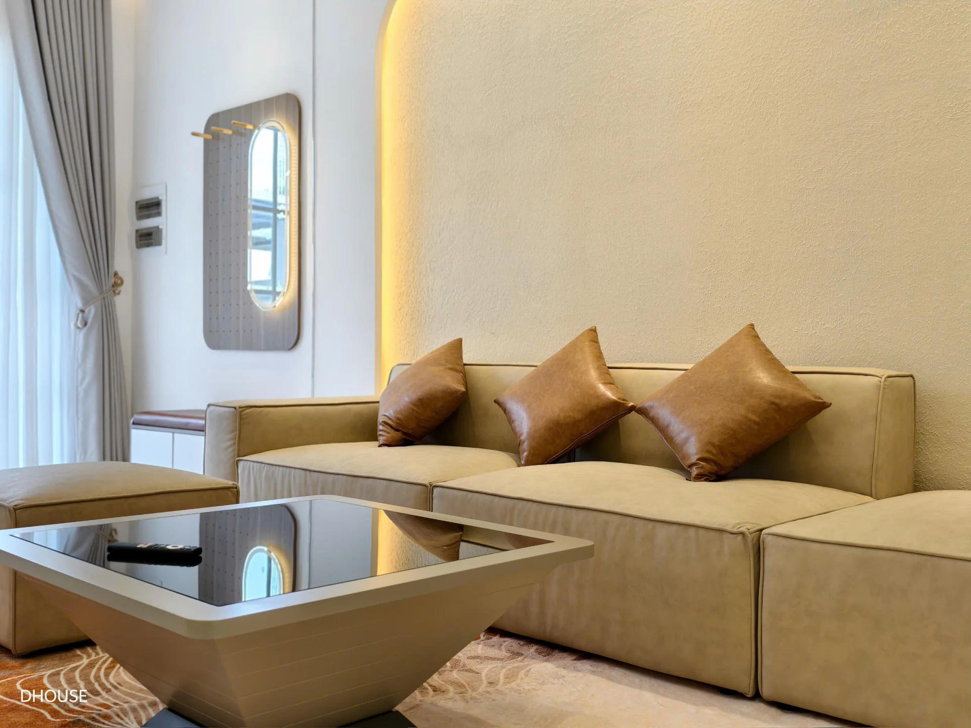 Ảnh thực tế phòng khách với sofa bọc vải màu be, gối nâu và bàn trà mặt kính, công trình D.HOUSE tại NovaWorld Phan Thiết