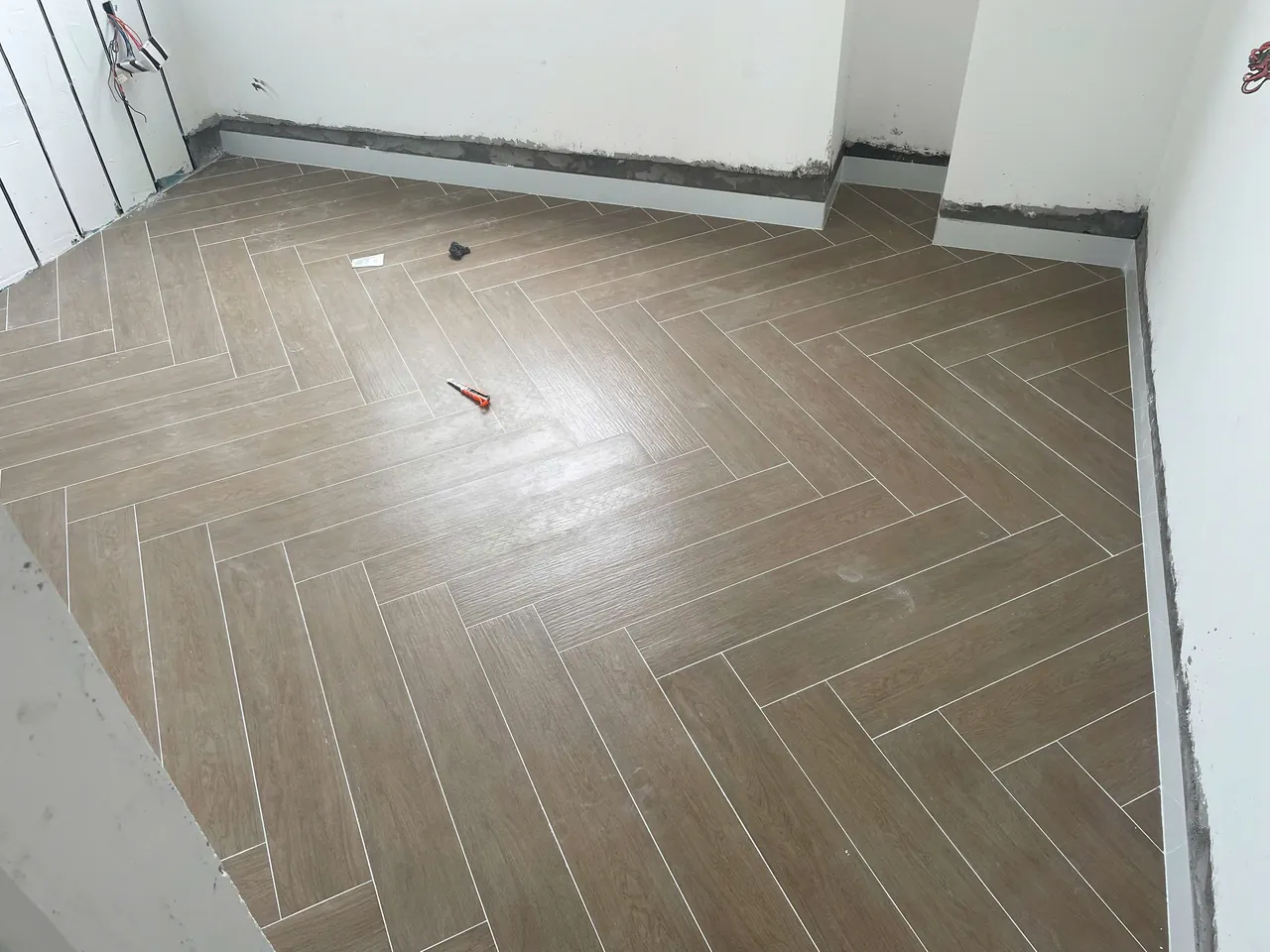 Sàn gạch vân gỗ lát kiểu xương cá, len chân tường đã gắn, tường còn chờ hoàn thiện